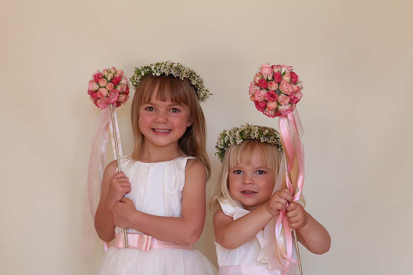 two cute flower girls hold pink flower wands with ribbon
