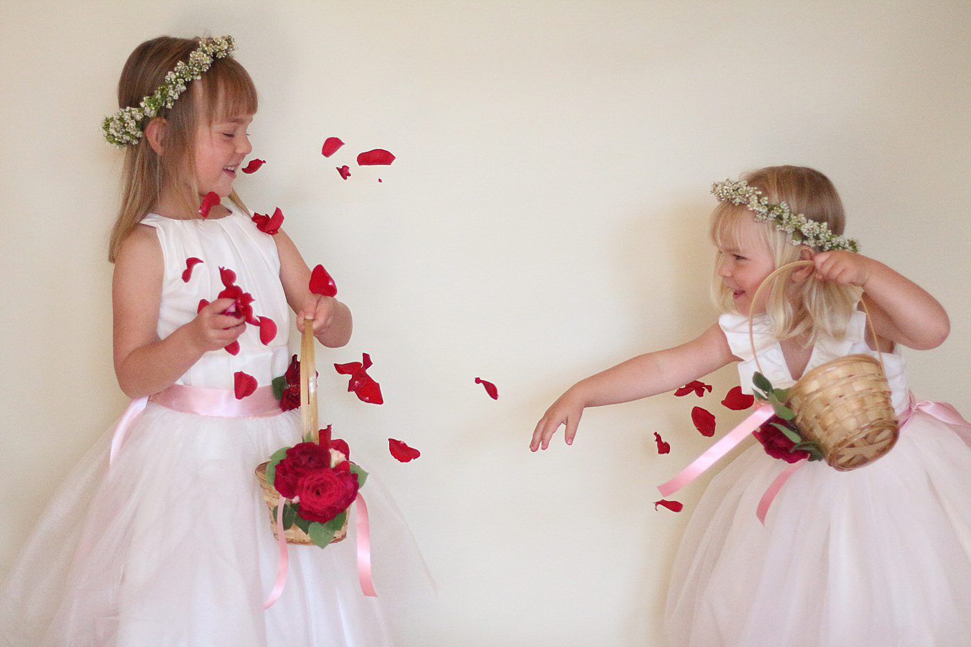 a flower girl thropwing red rose petals at another flower girl