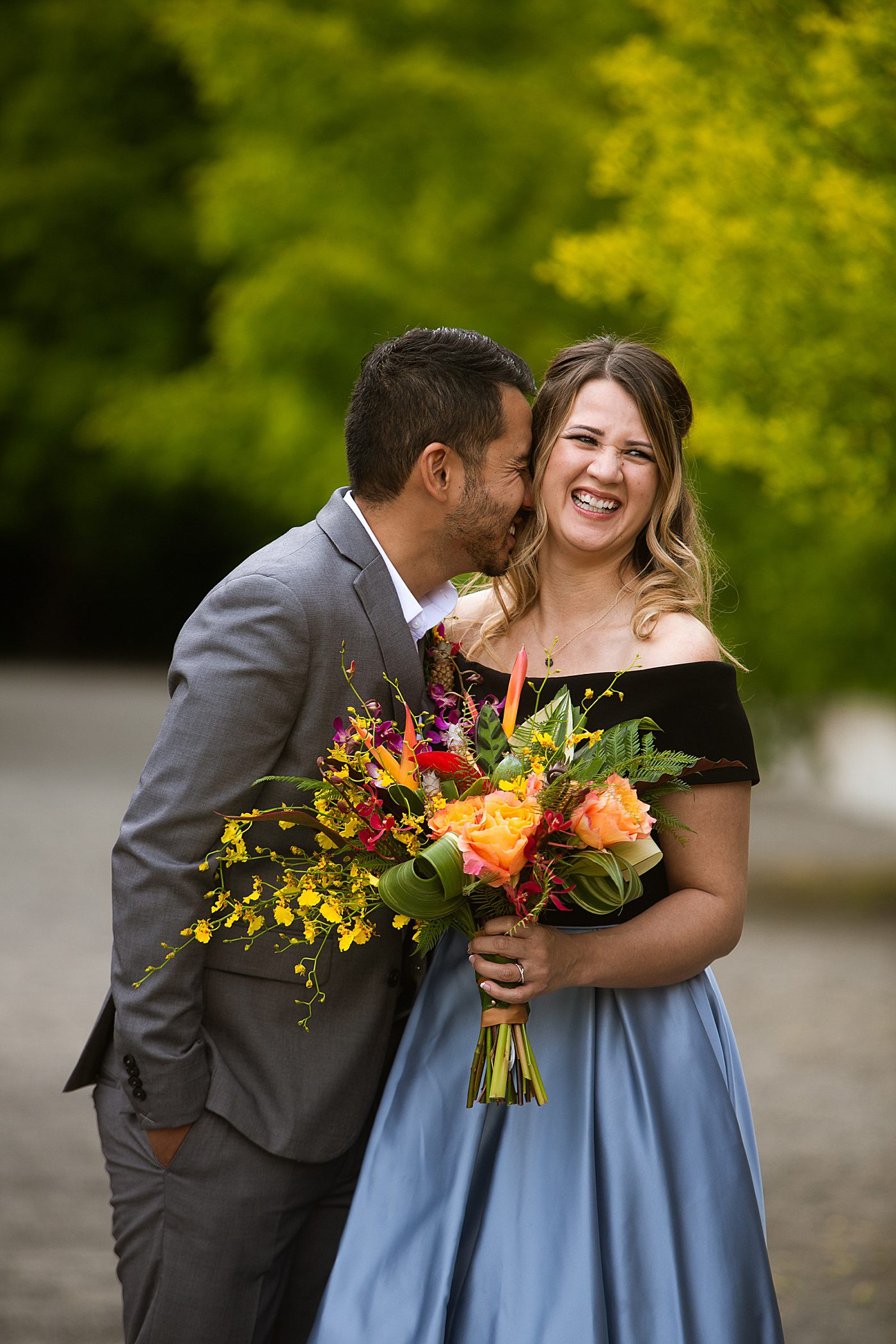 groom kissing bride holding colorful bouquet