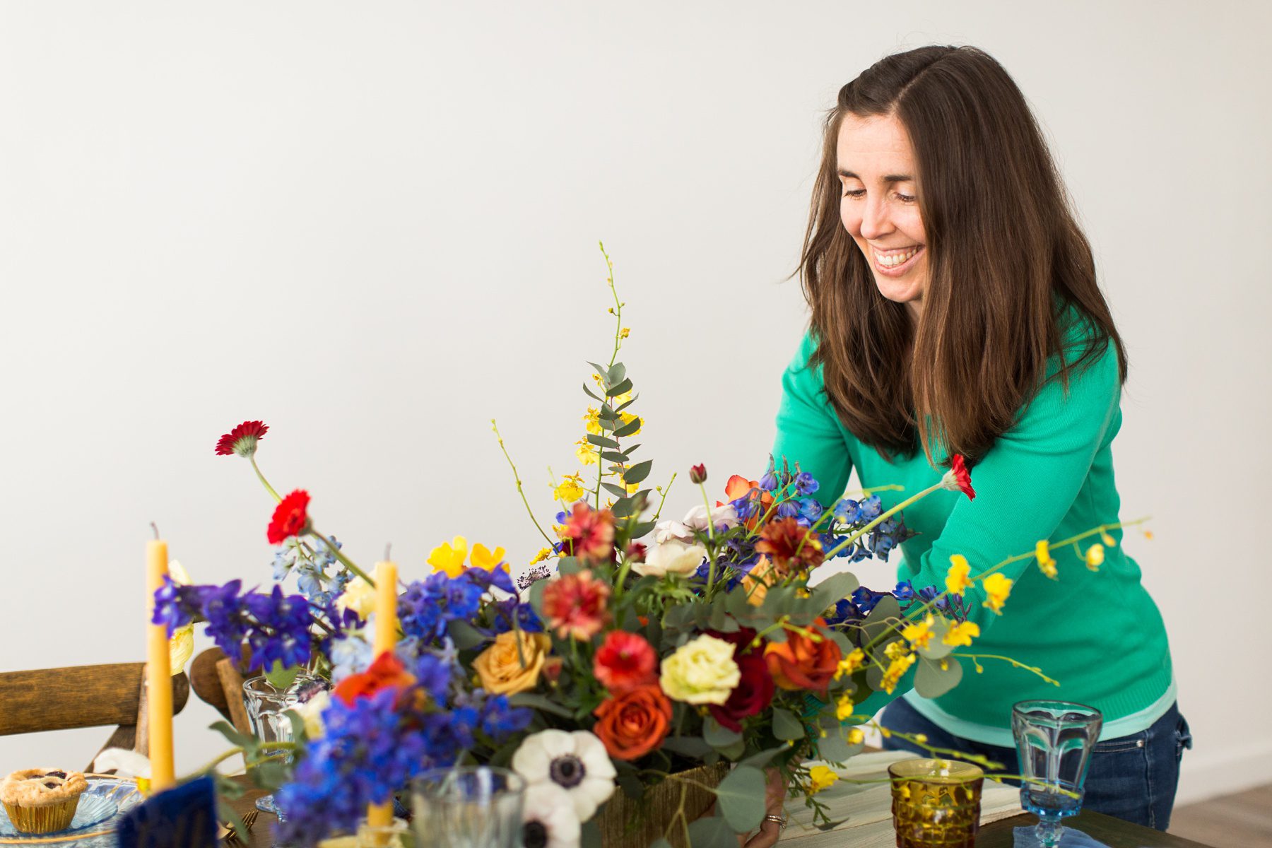 a lady in a geen top puts a floral arrangement on a table