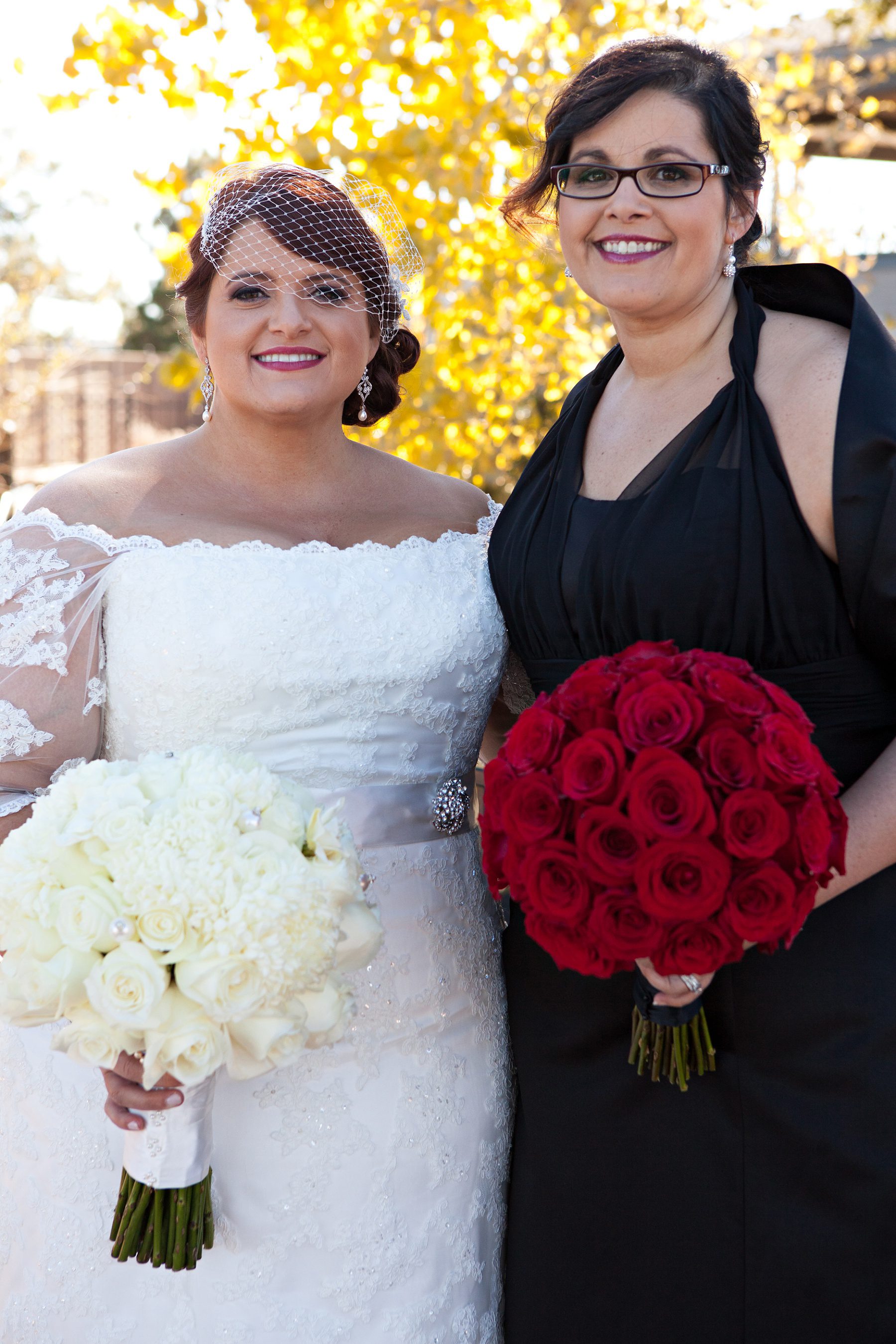 a bride and her bridesmaid holding red and white bouquets