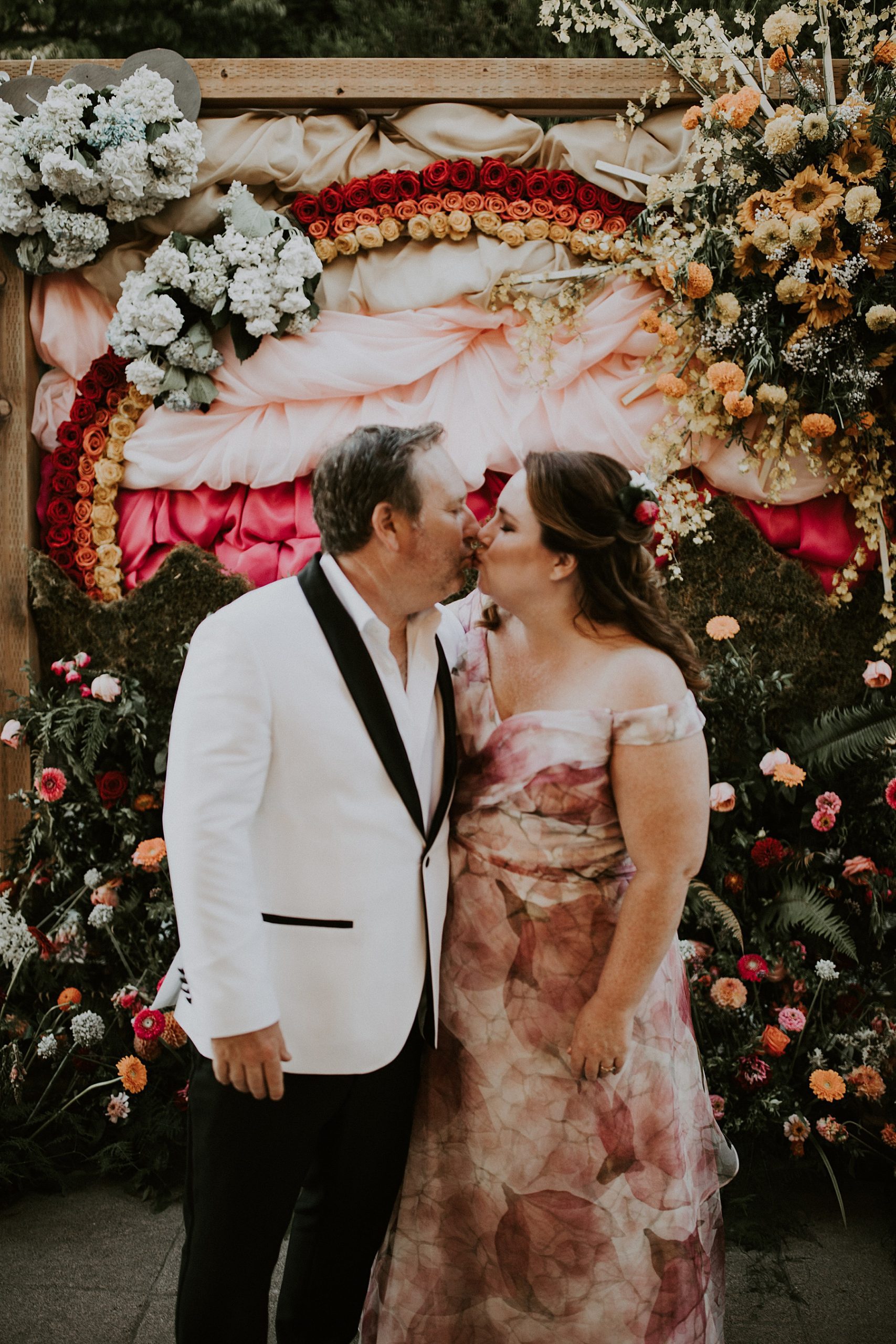 bride and groom kissing in front of a flower wall