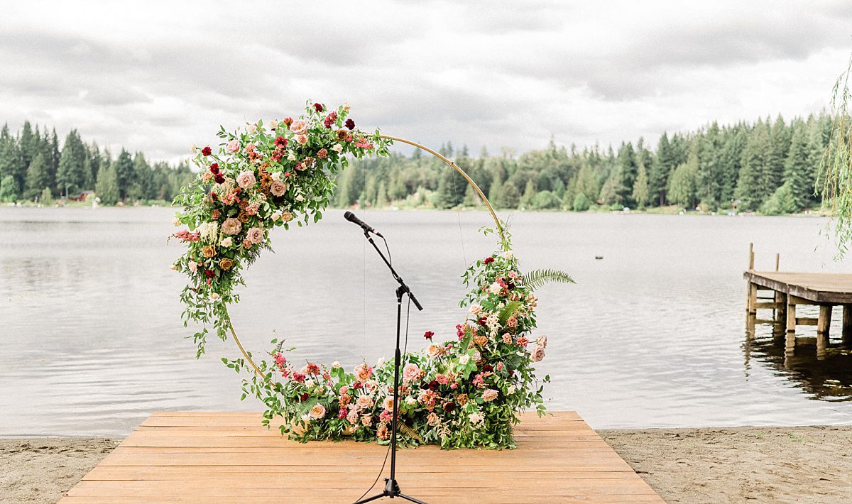 a circle wedding arch next to a lake with pink and white flowers