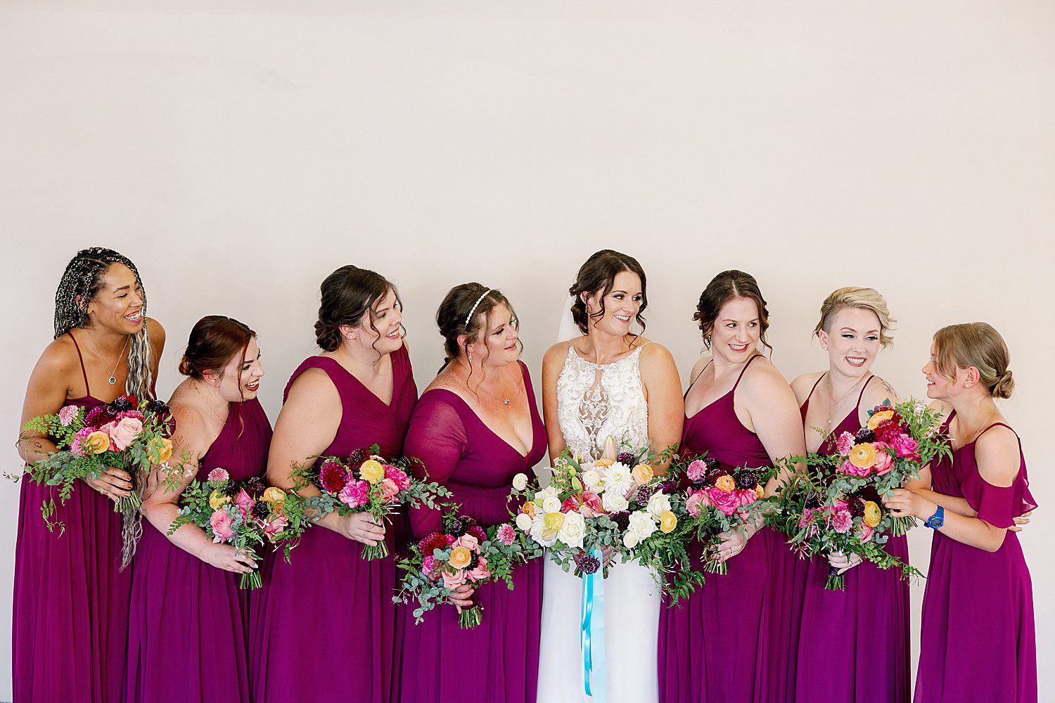 bridesmaids wearing plum dresses holding rich jewel-tones bouquets