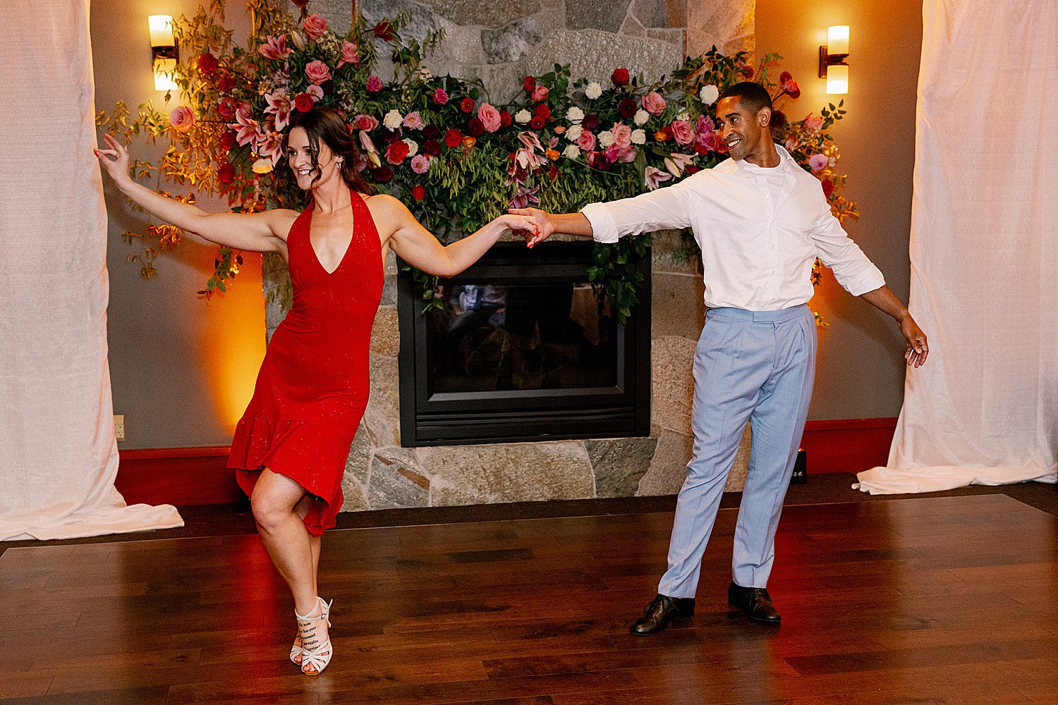 a woman in a red dress dances with a man in front of colorful mantle florals