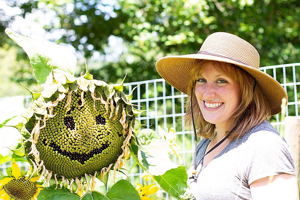 woman in hat next to a sunflower