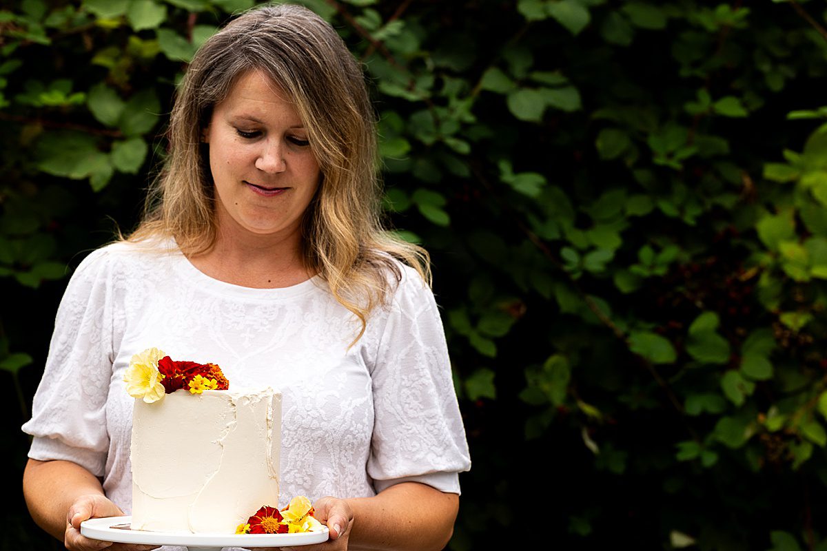 a lady holding a white cake with red, orange, and yellow fresh flowers on top