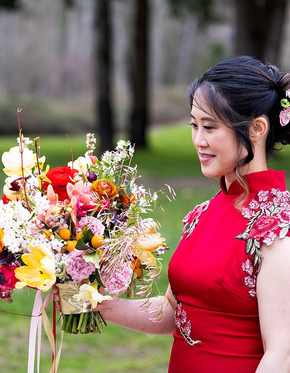 A Chinese bride in a red dress looks at a colorful bridal bouquet