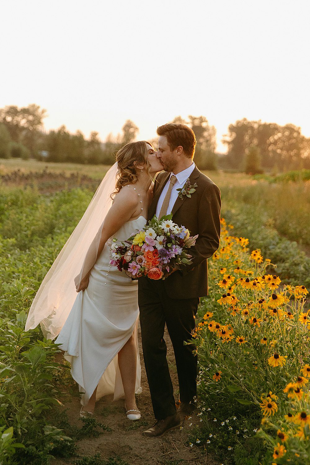 bride and groom are kissing in a field of yellow flowers during sunset