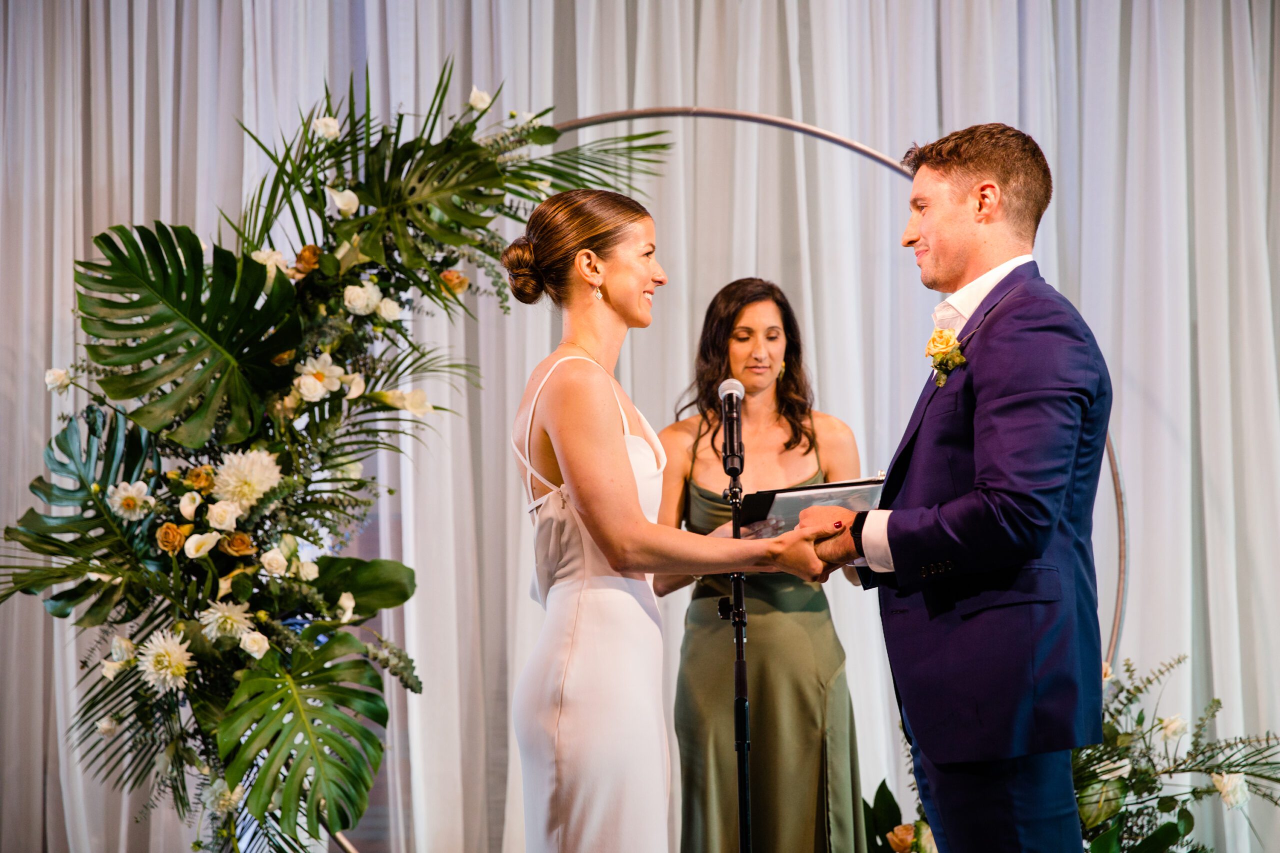 a bride and groom stand in front of a circle arch with palm fronds and white flowers