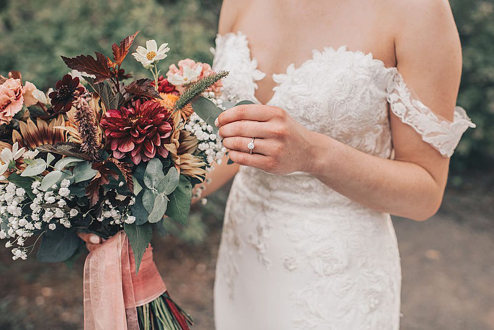 a woman in an off the shoulder wedding dress holds a sunflower and baby's breath bouquet