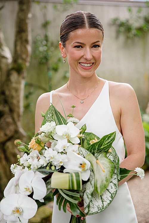 bride wearing a asymmetrical dress holds a tropical bouquet