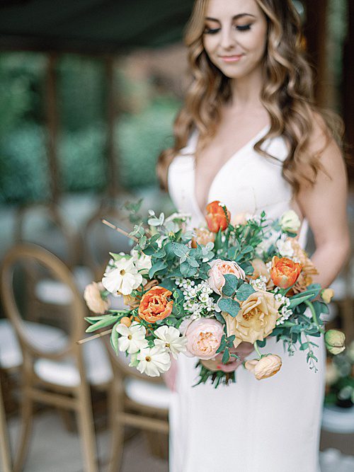 a bride holds a wedding bouquet with peach roses and eucalyptus