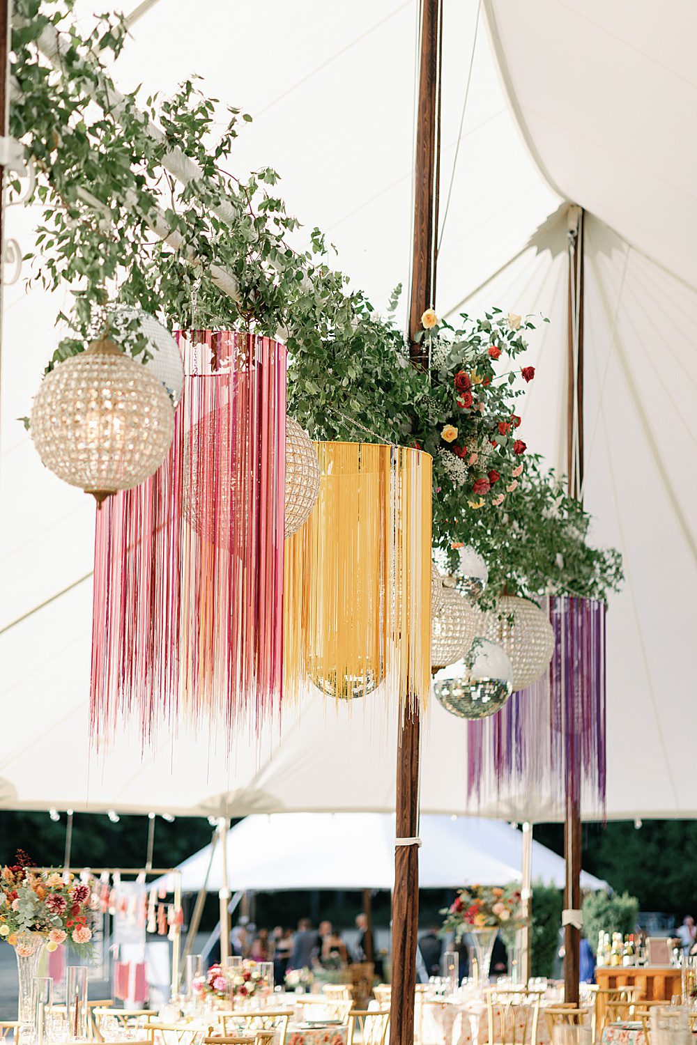 colorful hanging fringe decor with disco balls and greenery in a tent