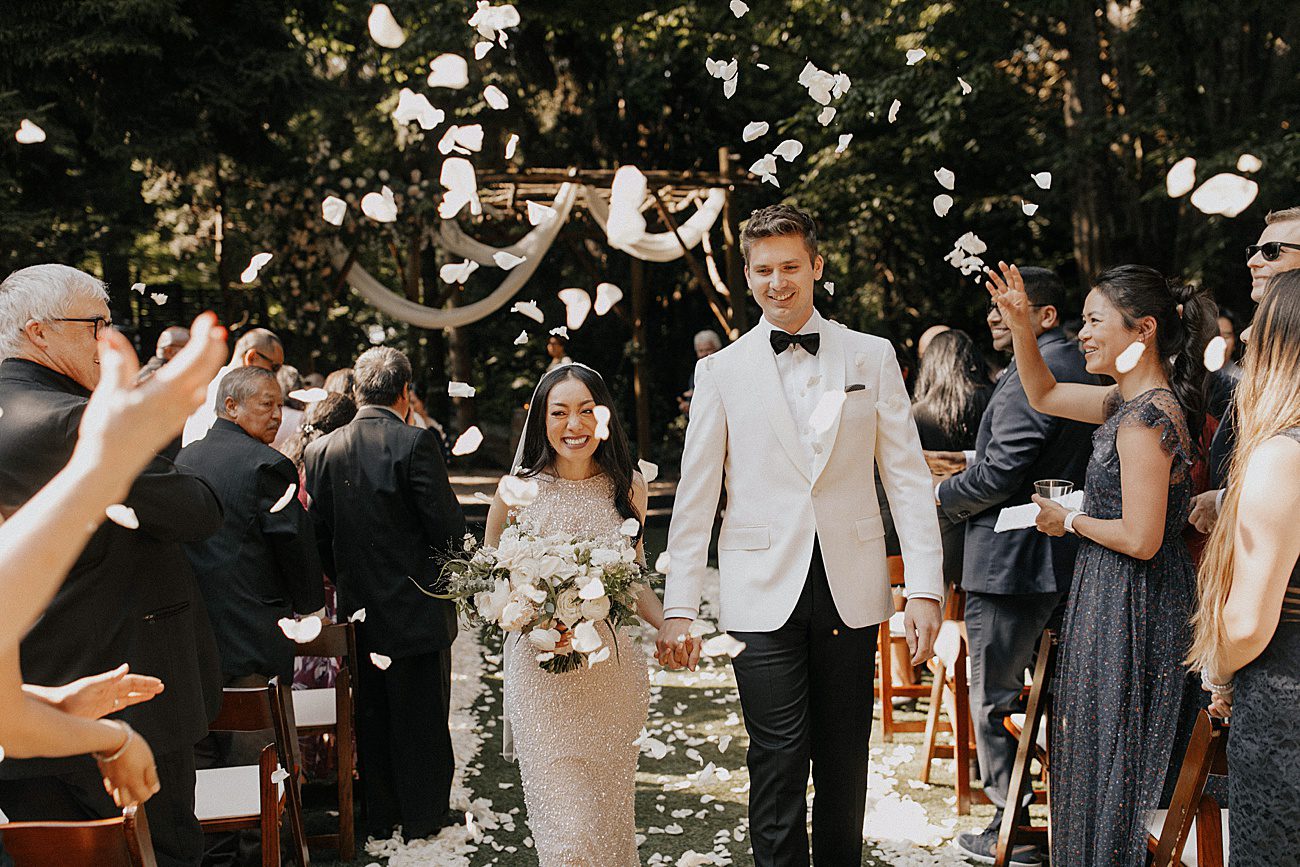 bride and groom walk down the aisle with guests throwing flower petals